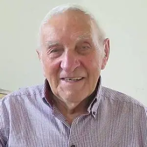 Ludwig Wiedemayr mit freundlichem Lächeln, trägt ein kariertes Hemd und sitzt vor einer hellen Wand.